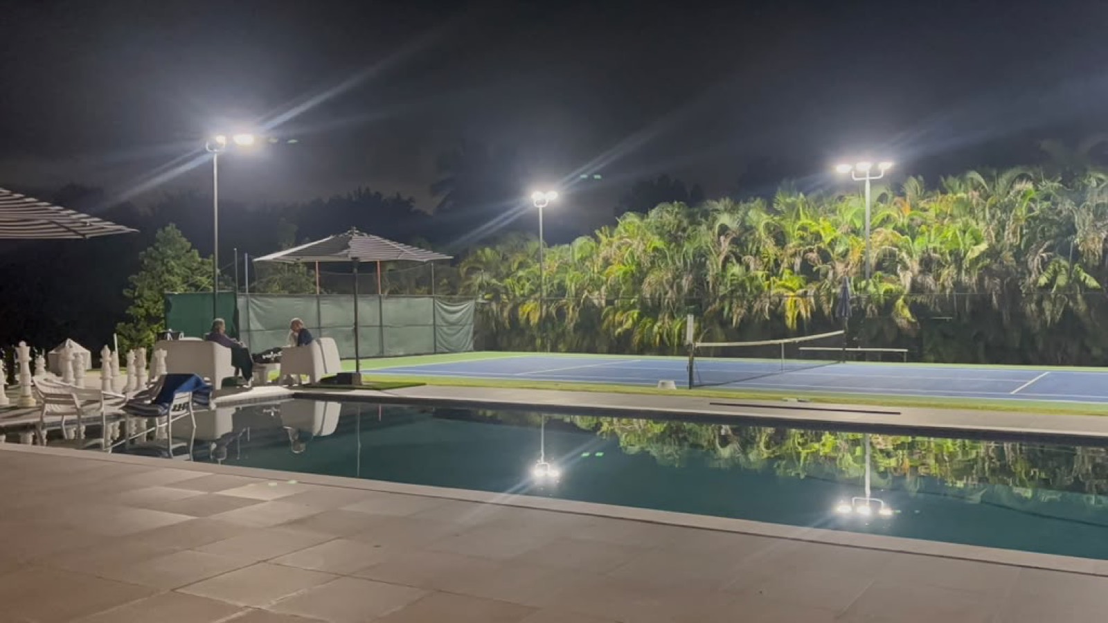 Cancha de tenis nocturna junto a una piscina