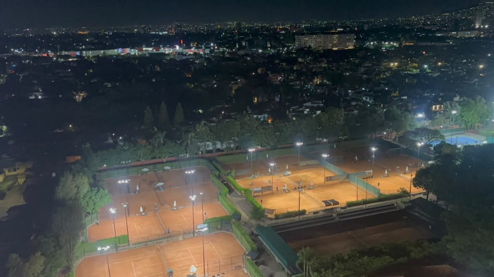 Vista aérea nocturna de canchas de arcilla iluminadas